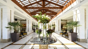 A spacious lobby with a high ceiling, a central round table with vases, and potted plants. - Miraggio Thermal Spa Resort (Kassandra)