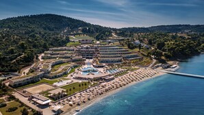 An aerial view of a coastal resort with multiple buildings, a central pool area, and a beach with umbrellas. - Miraggio Thermal Spa Resort (Kassandra)