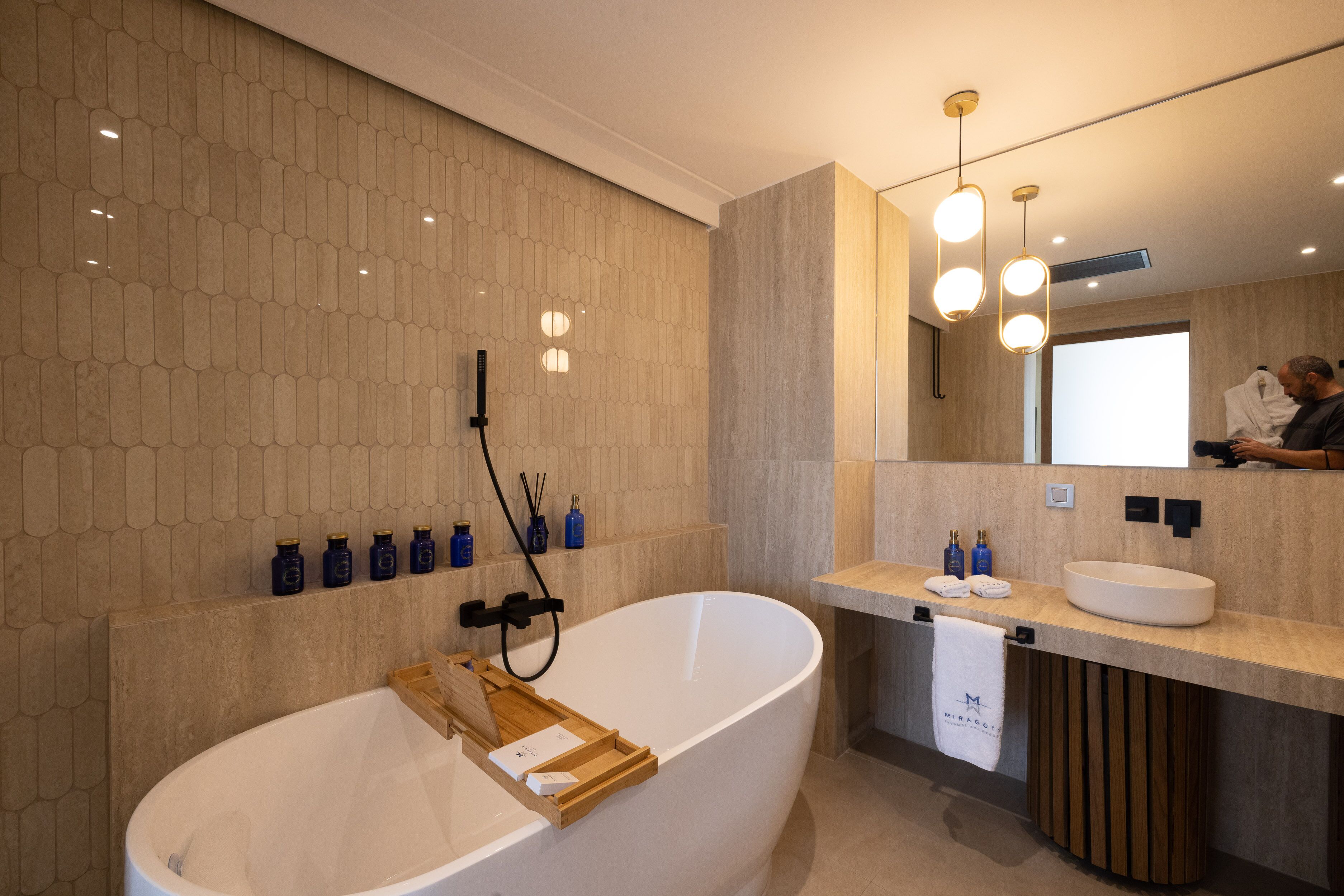 A modern bathroom with a freestanding bathtub, a large mirror, and a countertop with a sink and toiletries.