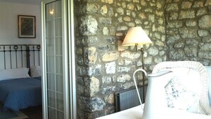 A bedroom with a stone wall, a bed with a blue polka dot bedspread, a white lamp, and a framed picture on the wall. - Hotel Los Caspios (Colunga)