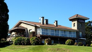 A large stone building with a prominent tower and a covered patio area. - Hotel Los Caspios (Colunga)