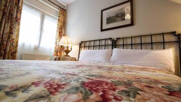 Una camera da letto con una coperta a fiori, una testiera classica, una lampada da comodino e un quadro appeso al muro.