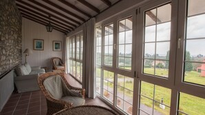 A covered porch with wicker furniture, large windows, and a stone wall. - Hotel Los Caspios (Colunga)