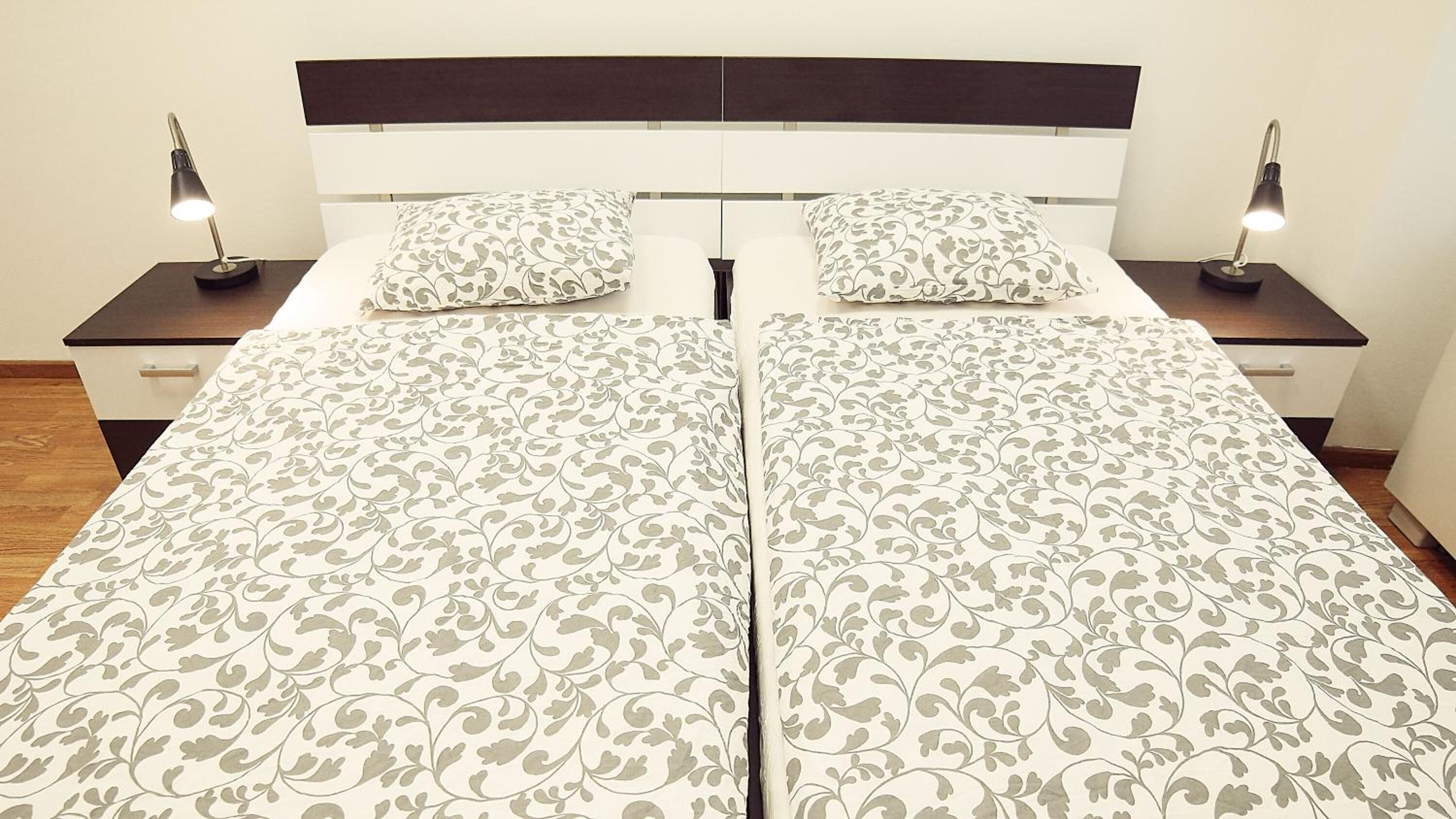 A double bed with a patterned bedspread, two bedside tables with lamps, and a dark headboard.