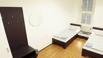 Quarto com duas camas de solteiro, um guarda-roupa, um espelho redondo e uma janela com persianas.