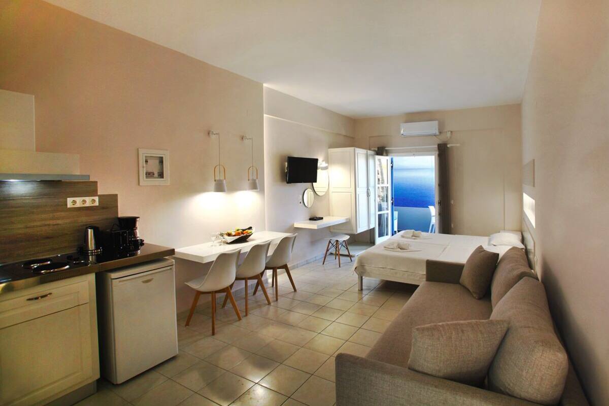 A compact hotel room with a kitchenette, a dining area, a sofa, and a TV.