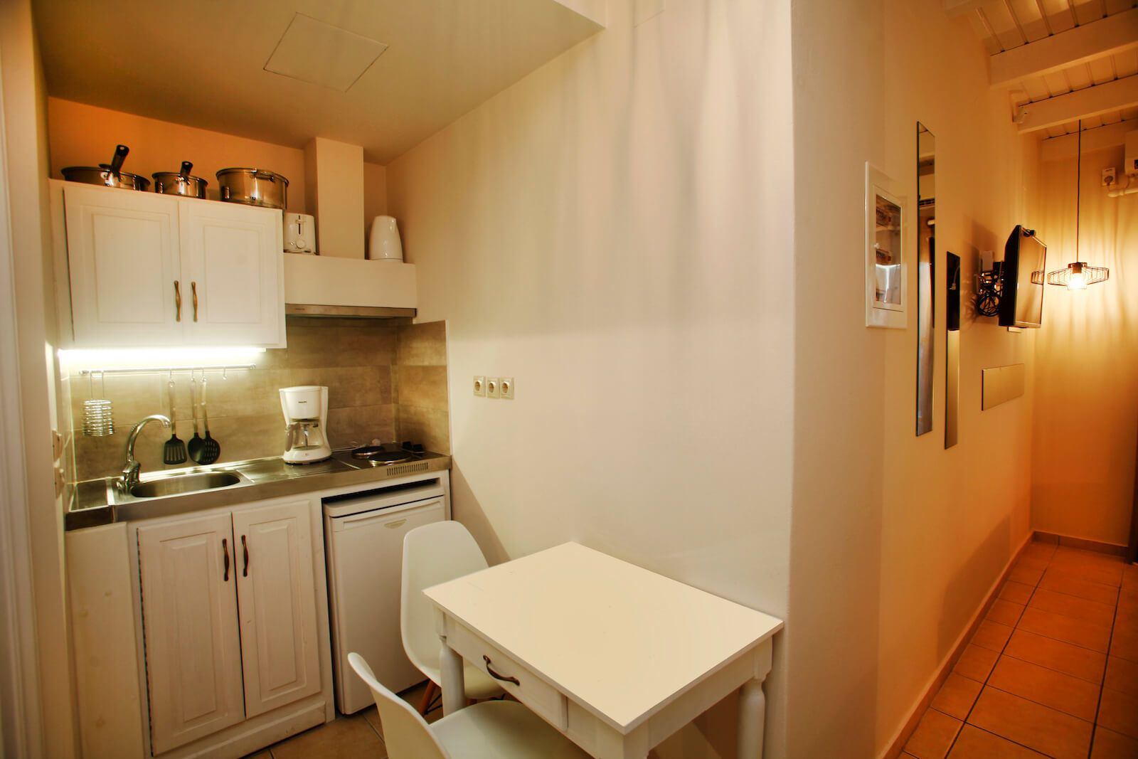 A compact kitchen with white cabinets, a sink, a stove, and a small dining table with a chair.
