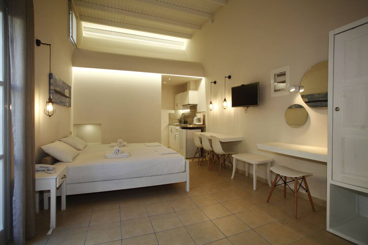 A bedroom with a bed, bedside table, desk, chair, and a TV mounted on the wall.