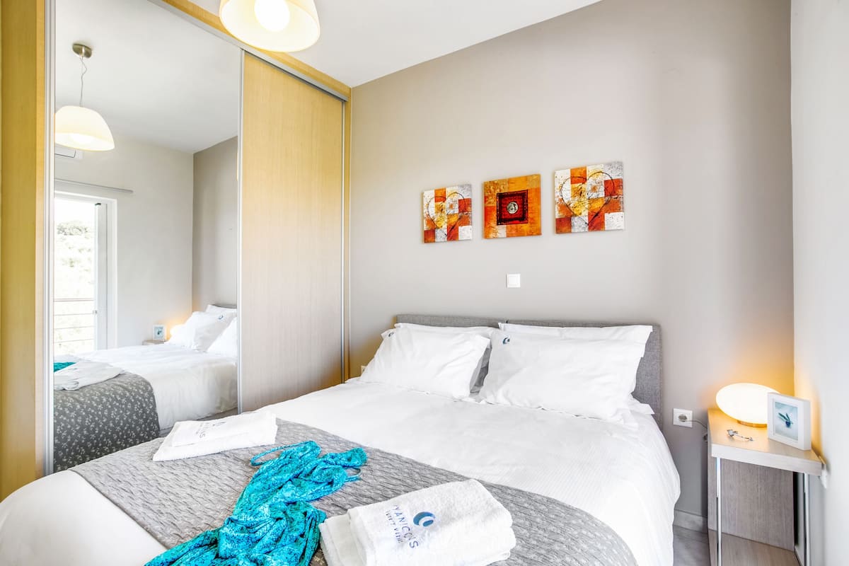 A hotel room with a bed, a bedside table with a lamp, and artwork on the wall.