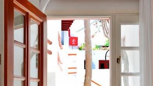 A room with a bed, a wooden door, and a view of a stone pathway leading outside. - Villa Pinelopi (Mykonos)