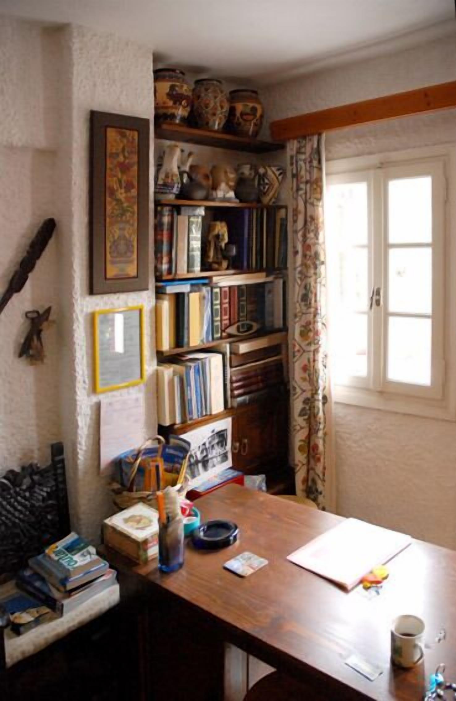 A cozy room with a wooden desk, bookshelves, and a window with curtains.