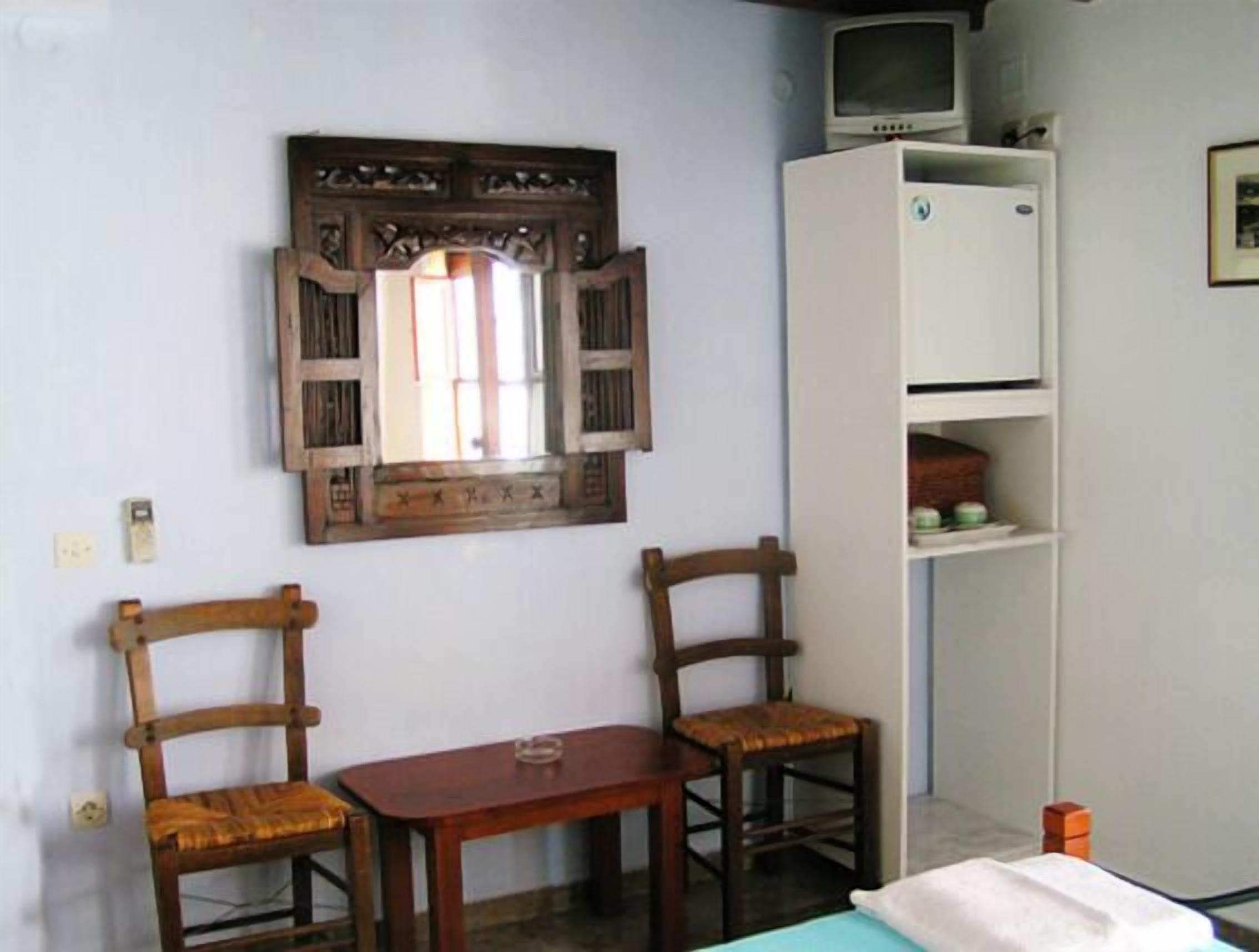 Una habitación con dos sillas de madera, una mesita de madera, un armario blanco y un televisor encima del armario.