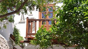 A courtyard with a white building, stone walls, a wooden door, and potted plants. - Villa Pinelopi (Mykonos)