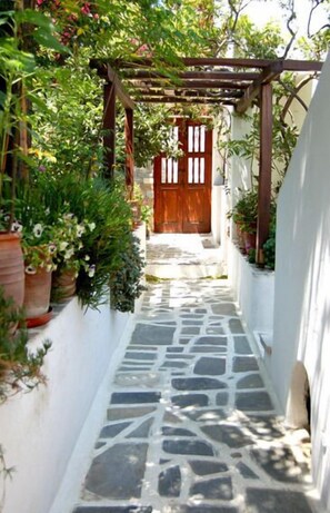 A narrow stone pathway leading to a wooden door, flanked by white walls and potted plants. - Villa Pinelopi (Mykonos)