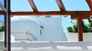 A balcony with wooden chairs, a white wall, and a clear blue sky. - Villa Pinelopi (Mykonos)
