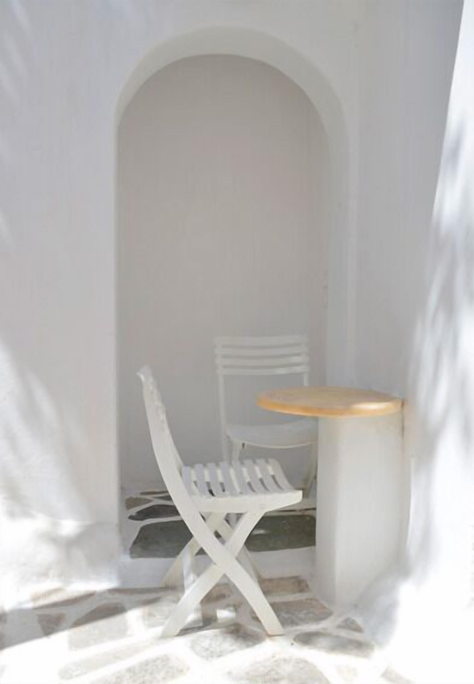 A small, enclosed outdoor seating area with a white chair and table, enclosed by a white archway.