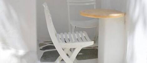 Un pequeño espacio al aire libre con asientos, que incluye una silla y una mesa blancas, delimitado por un arco blanco.