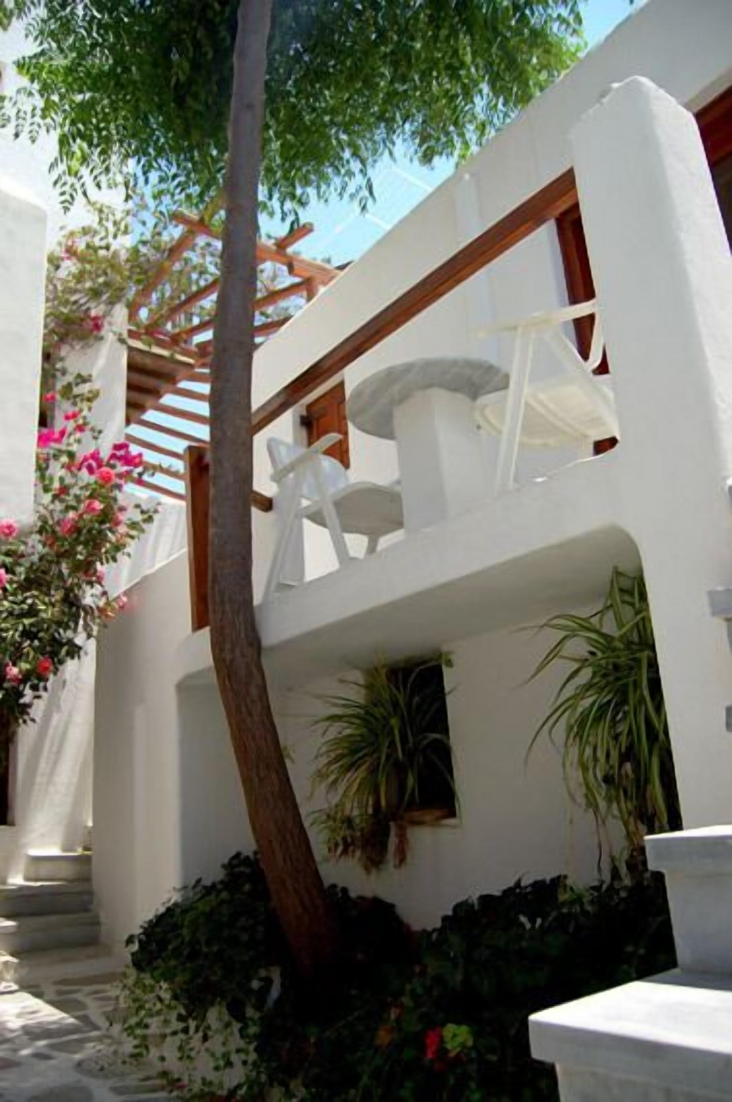 A white building with a balcony, a wooden pergola, and potted plants.
