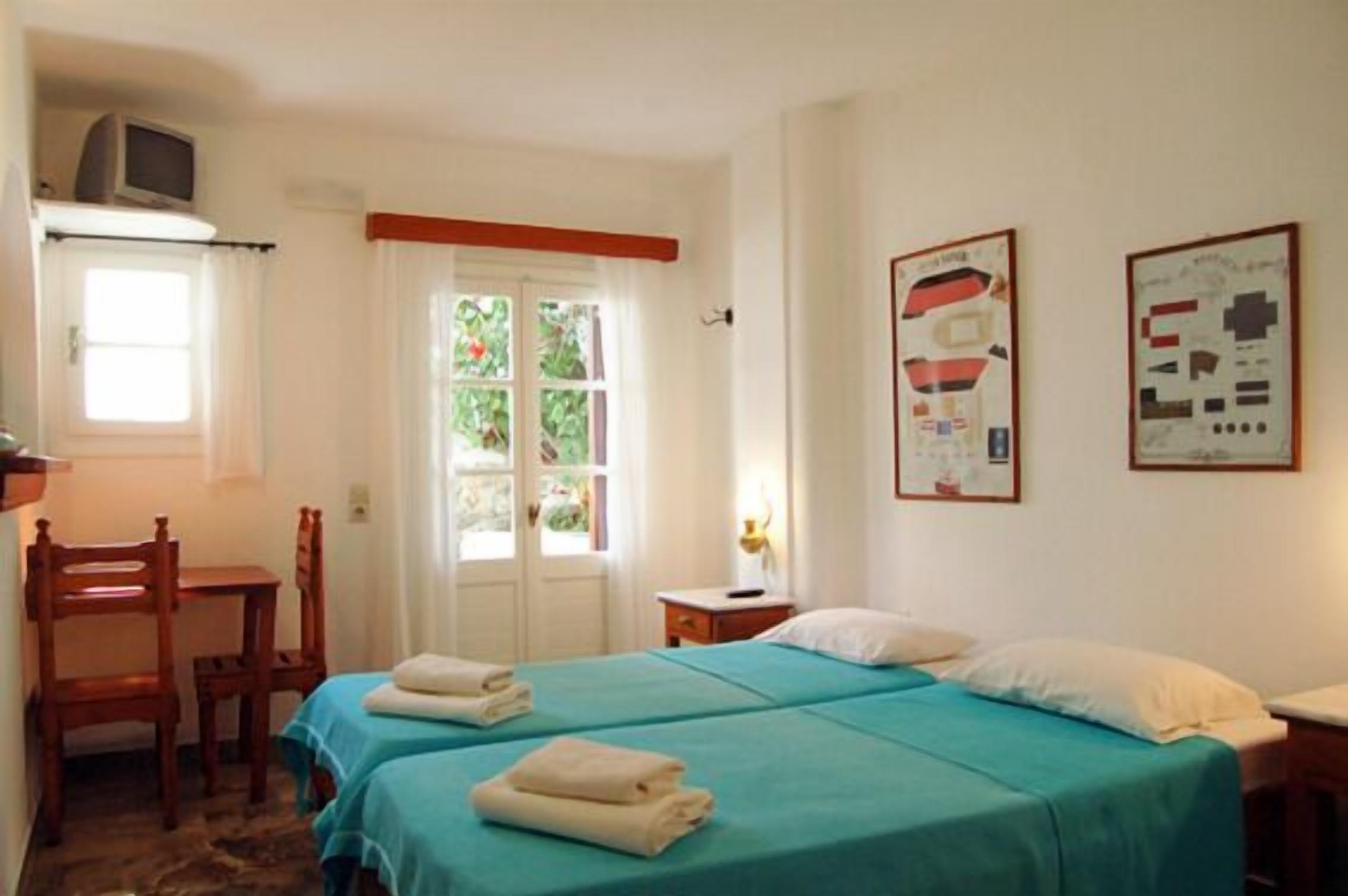 A room with two beds, a desk, a chair, and a window with curtains.