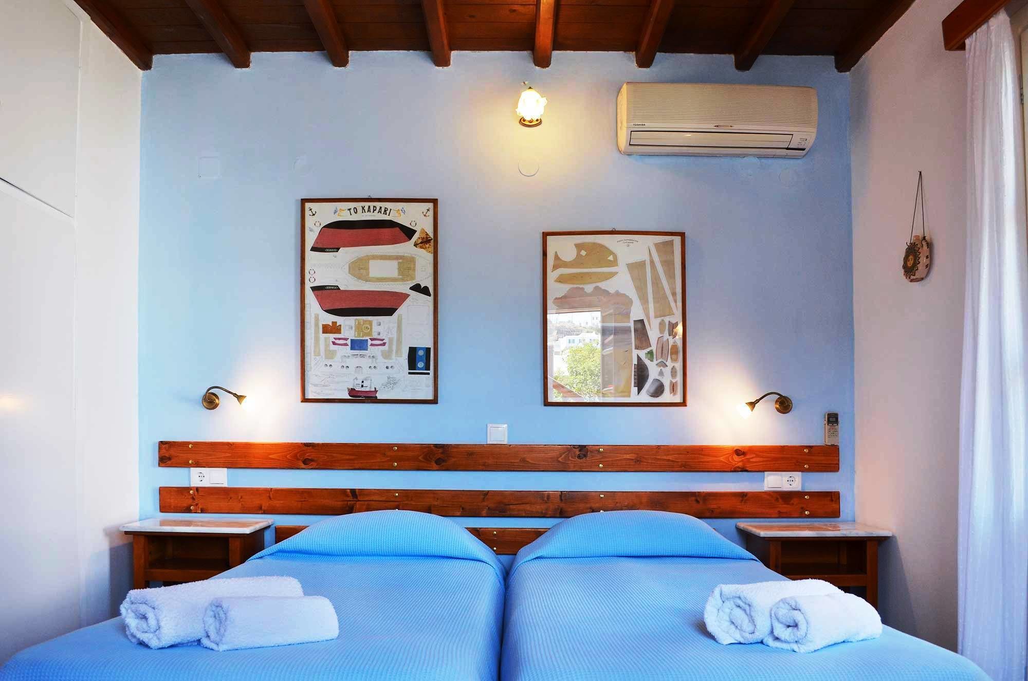 A room with two beds, a wooden headboard, a wall-mounted air conditioner, and two framed nautical charts.