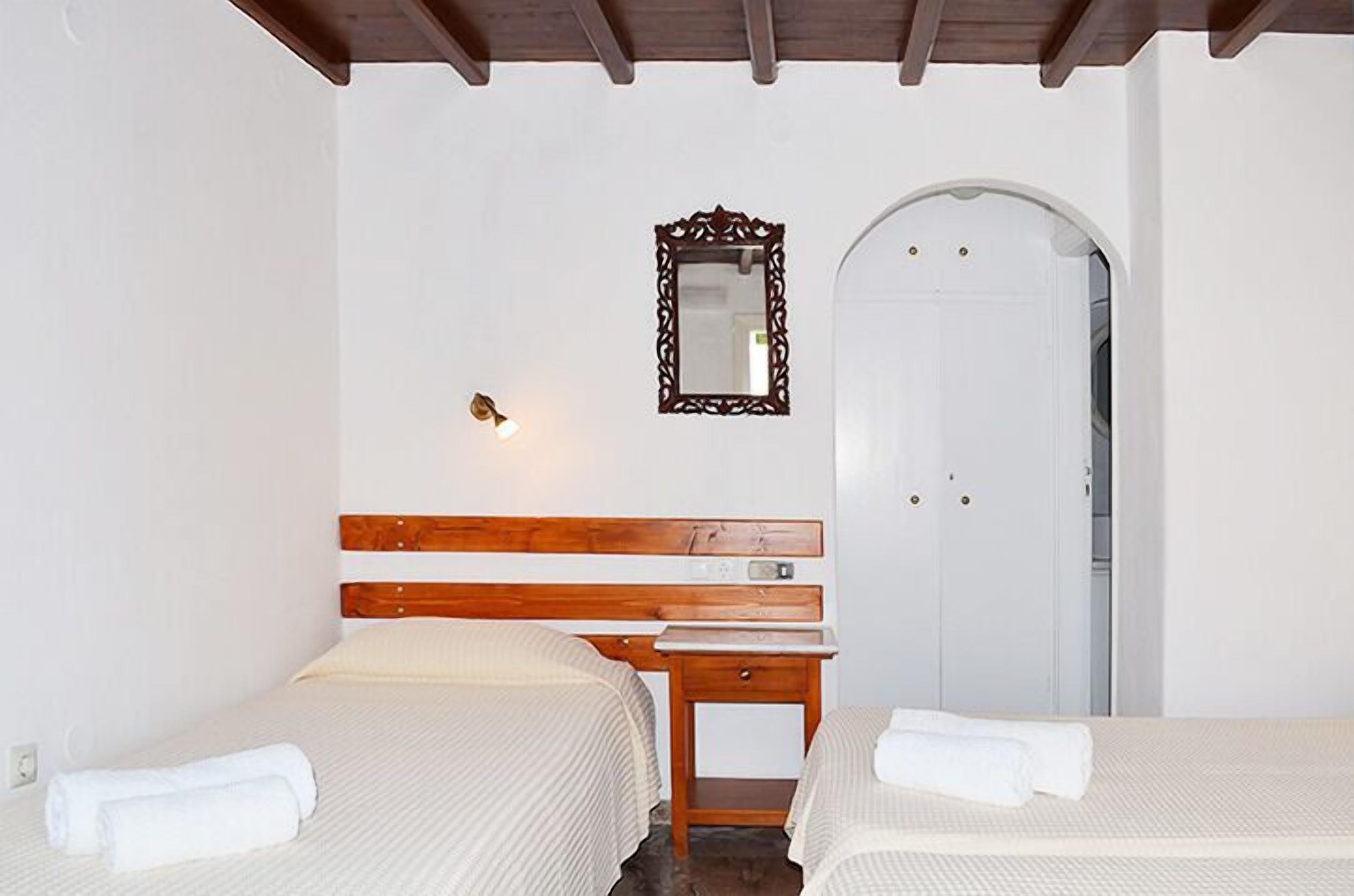 Une chambre d’hôtel avec deux lits, une tête de lit en bois, une table de chevet, un miroir et une porte blanche.