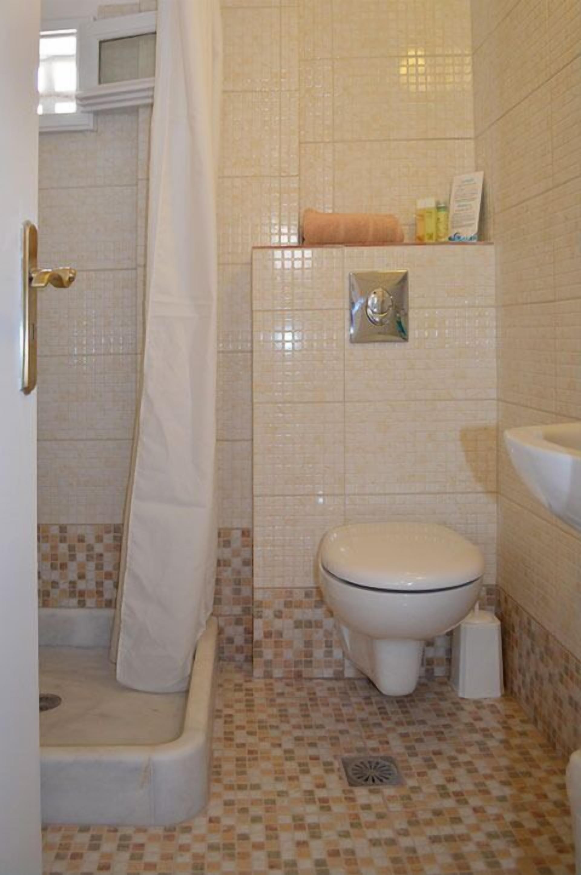 Une salle de bain avec douche, toilettes et carrelage au sol.