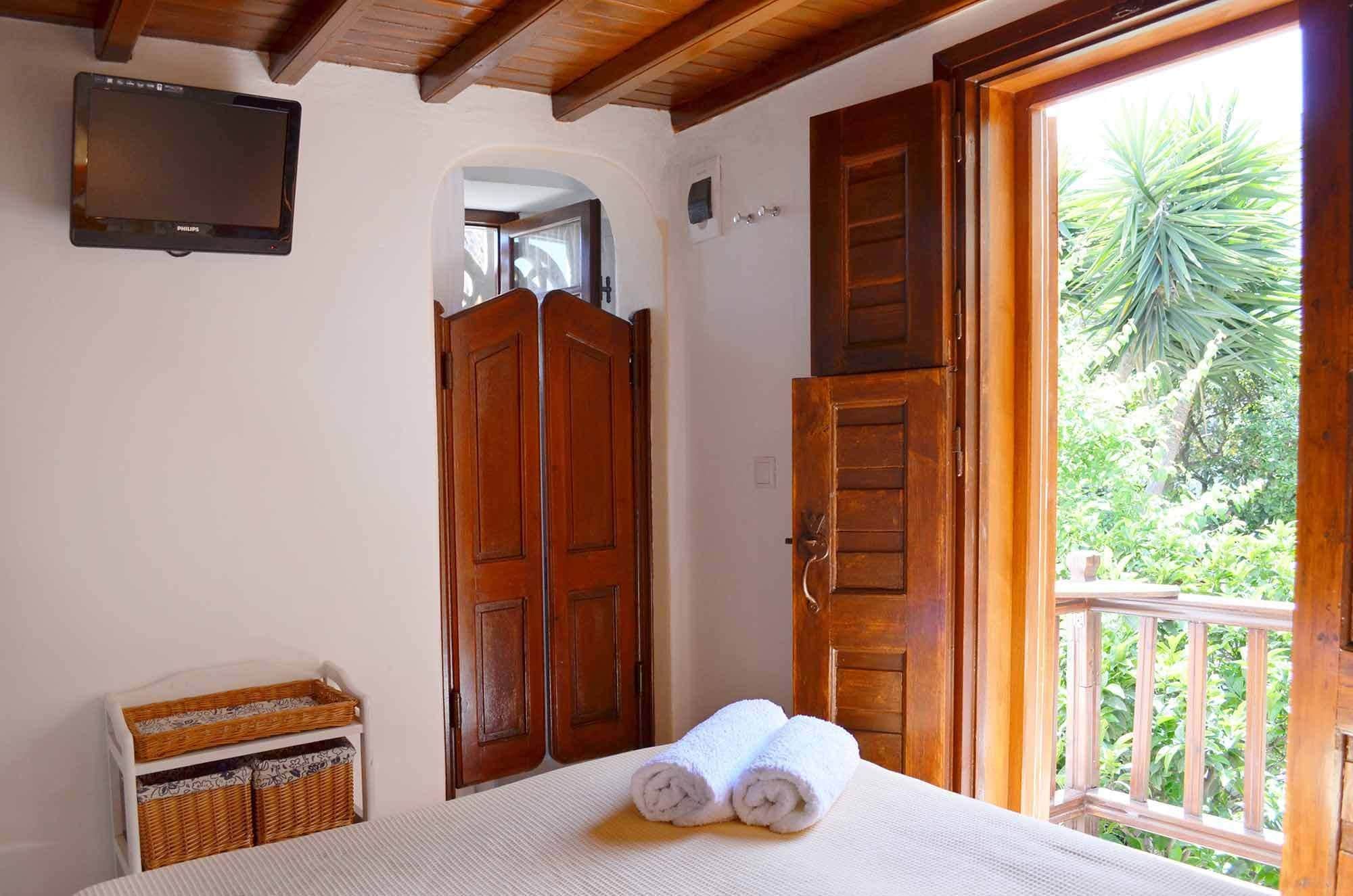 Un dormitorio con cama, puertas de madera, televisor y vista a zonas verdes.
