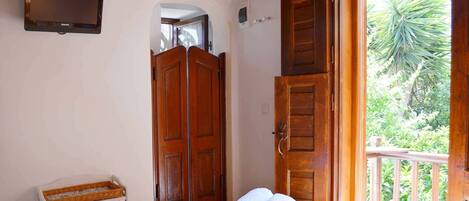 Un dormitorio con cama, puertas de madera, televisor y vista a zonas verdes.
