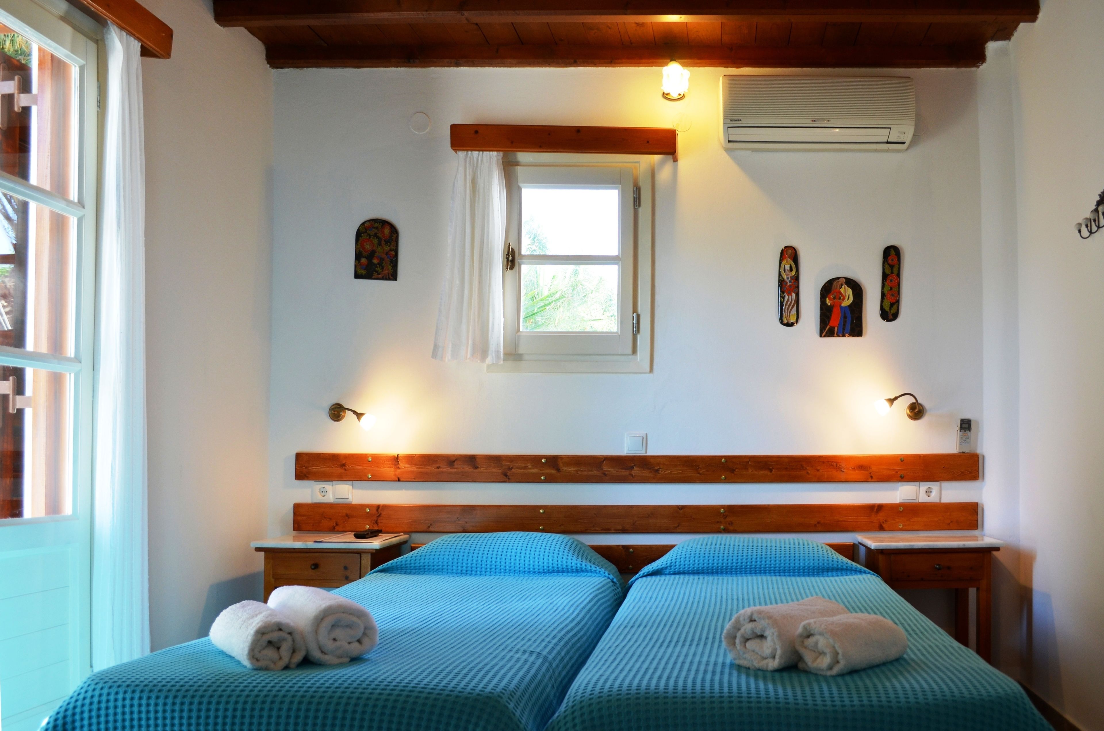 Habitación con dos camas, cabeceros de madera, una ventana pequeña con cortina y lámparas de pared.
