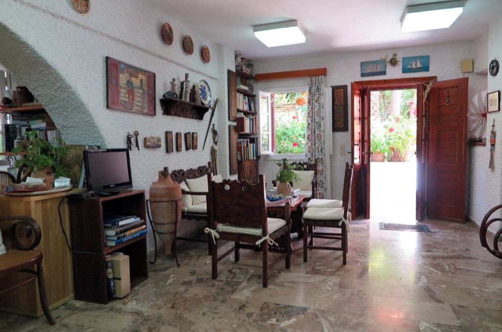 Una sala de estar acogedora con una mesa de centro de madera, un televisor y una estantería. Se ve una ventana con cortinas y una puerta que da al exterior.