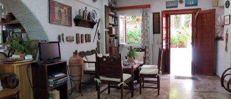 Una sala de estar acogedora con una mesa de centro de madera, un televisor y una estantería. Se ve una ventana con cortinas y una puerta que da al exterior.
