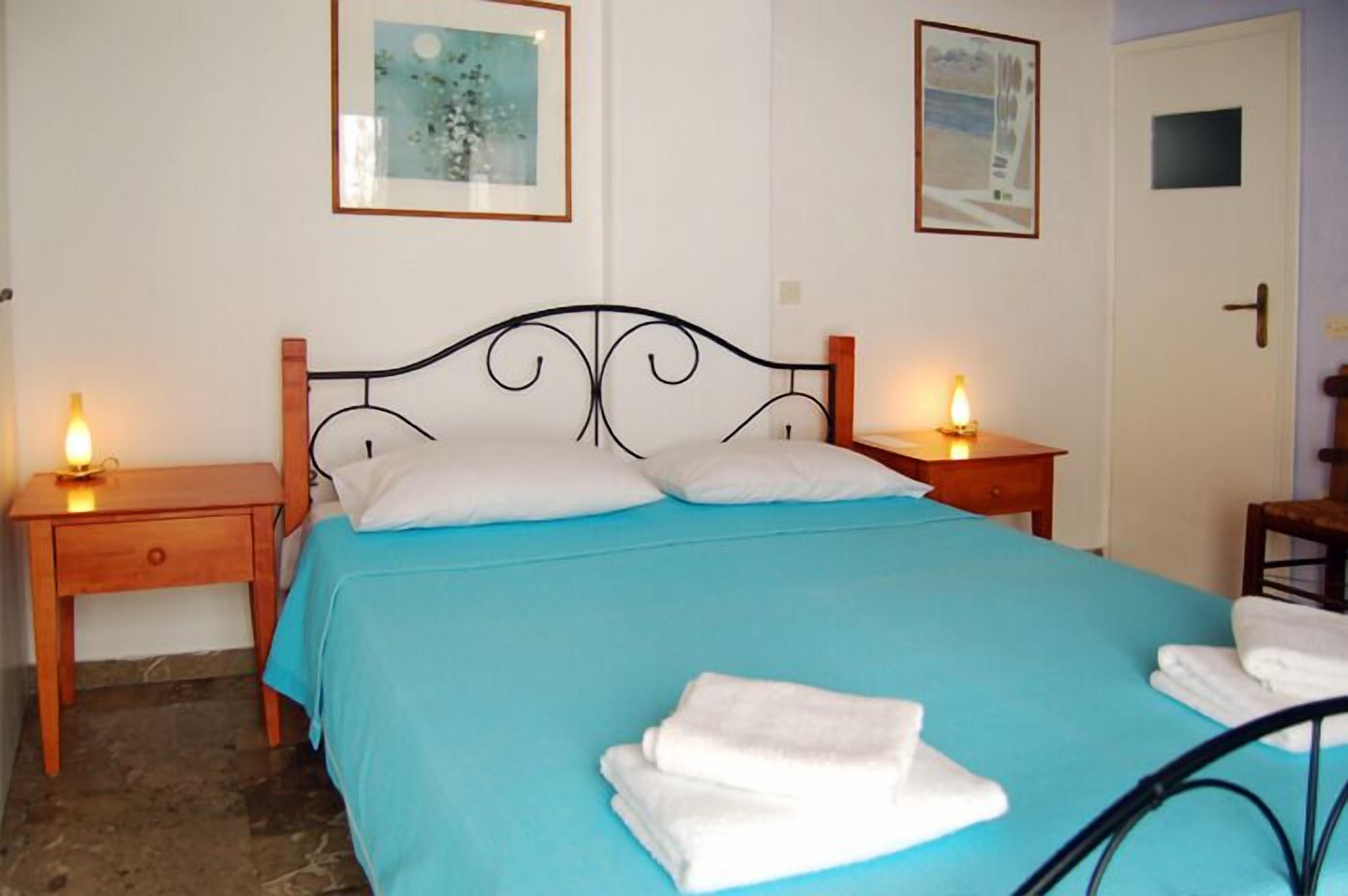 A bed with a blue bedspread, two bedside tables with candles, and a door with a small window.