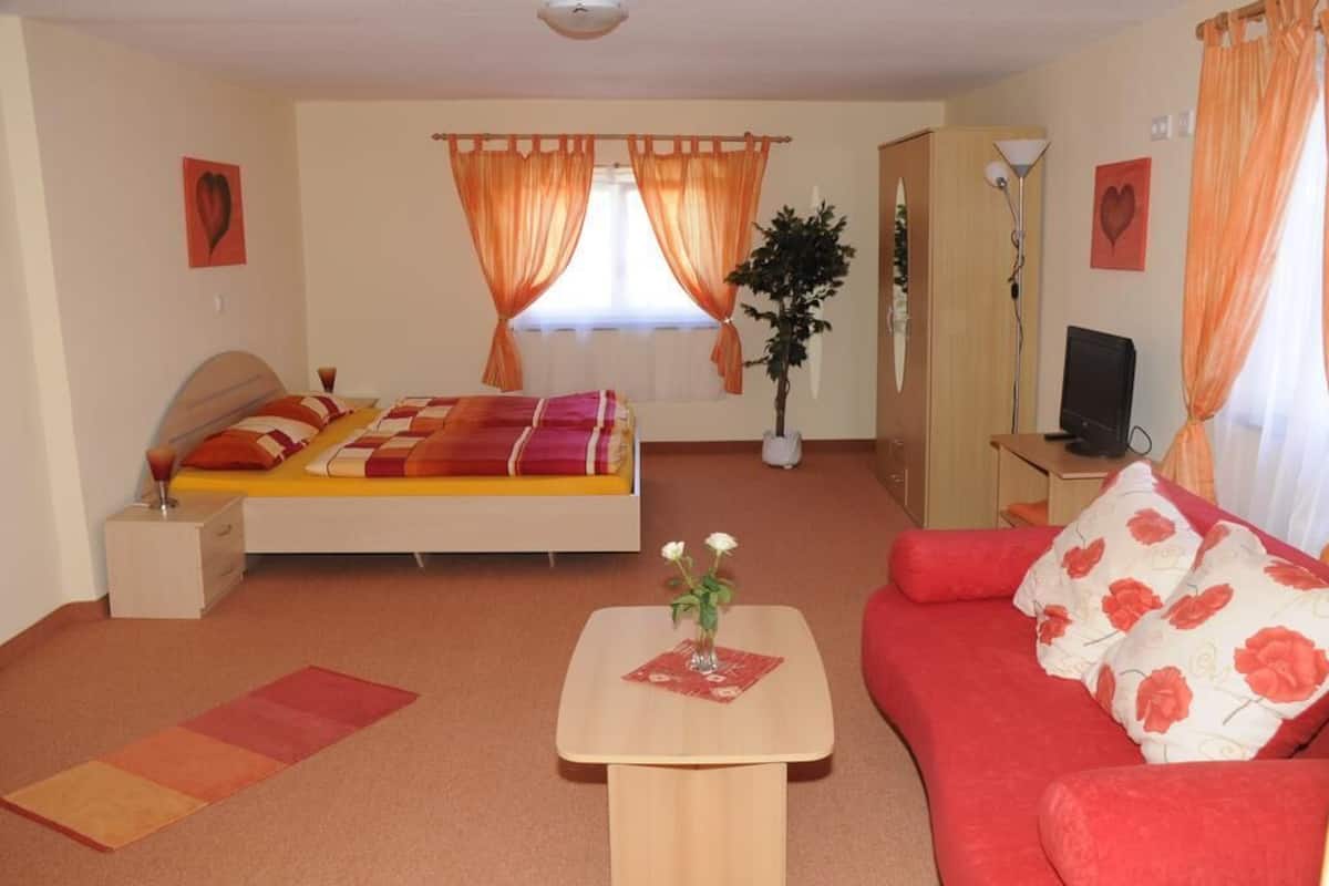 A bedroom with a bed, a red sofa, a small table with a vase, and a desk with a computer.