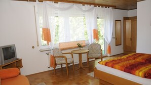 A room with a bed, a TV, a table with chairs, and a window with curtains. - Landgasthof Germania (Ruedesheim am Rhein)
