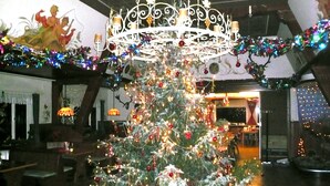 A Christmas tree decorated with lights and ornaments in a dining area with wooden chairs and a chandelier. - Landgasthof Germania (Ruedesheim am Rhein)