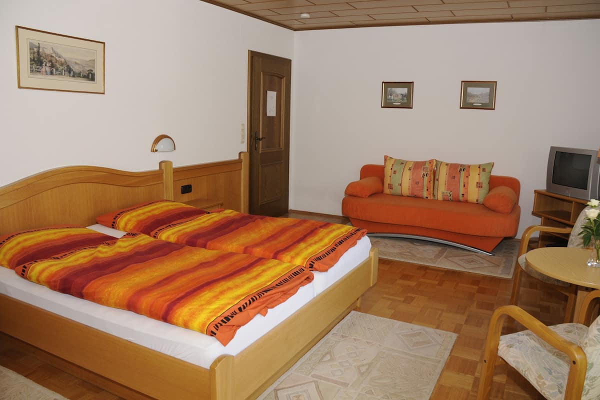 A bedroom with a wooden bed, an orange sofa, a television, and a small table with a vase.