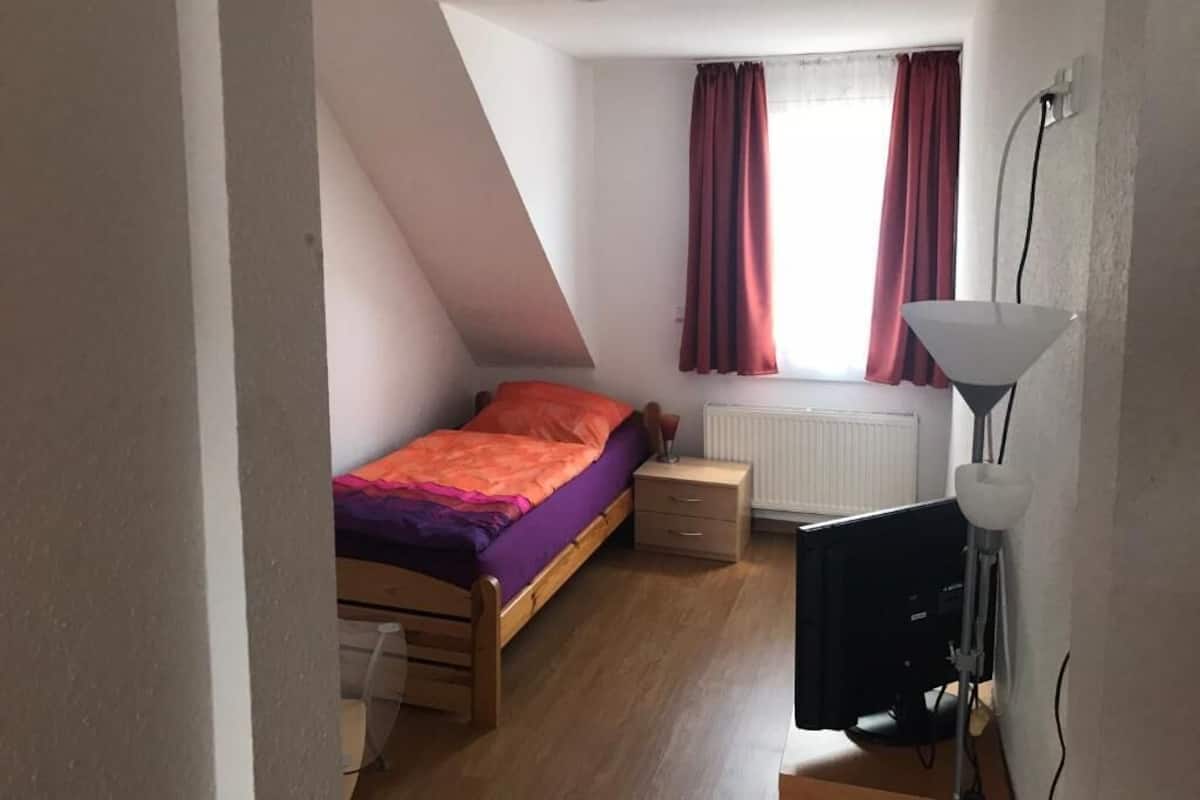 A bedroom with a bed, a desk, a lamp, and a window with curtains.