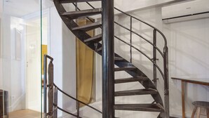 Una escalera de caracol con barandillas de vidrio y estructura metálica, que conduce a un piso superior.