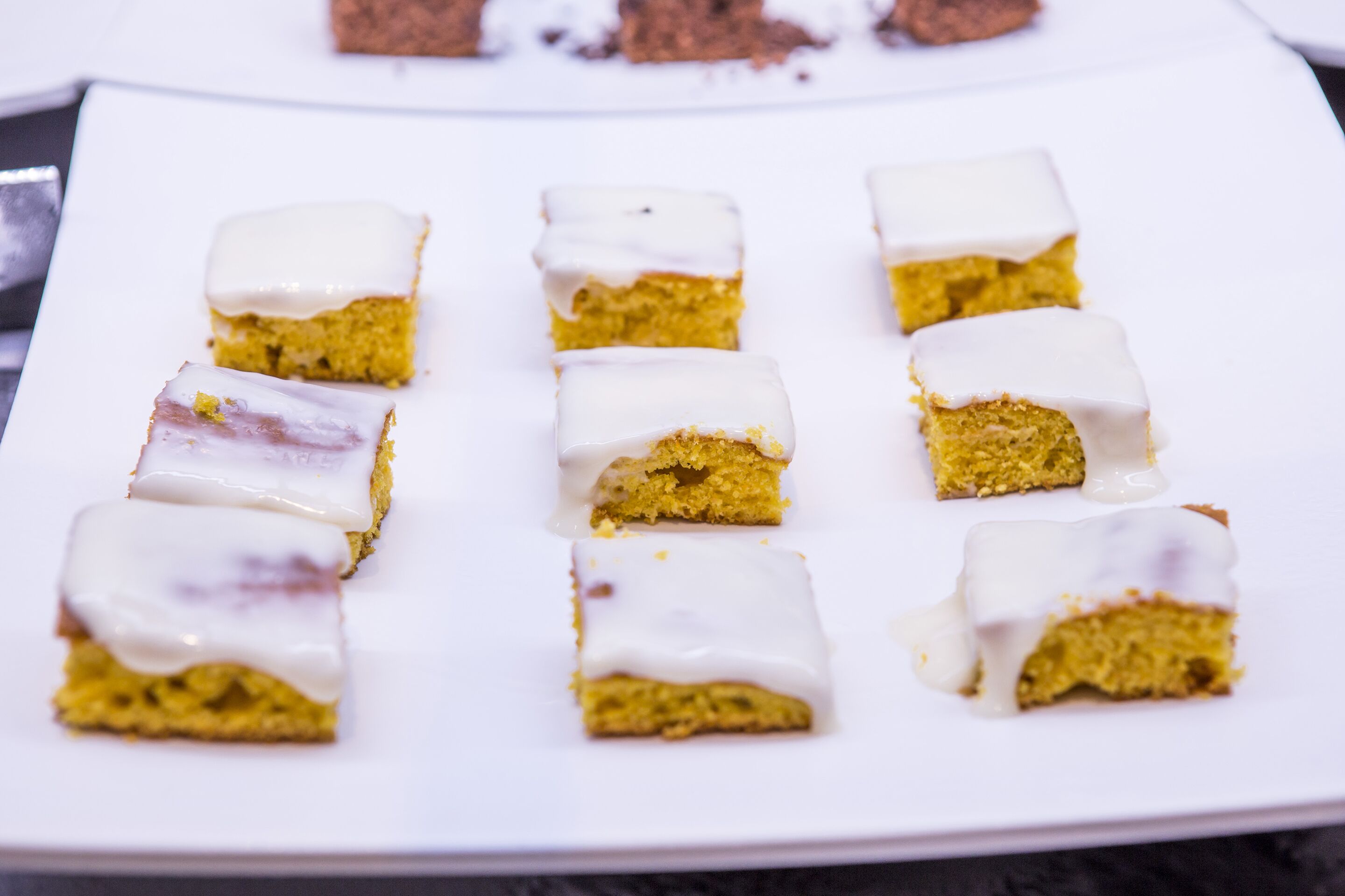 Une assiette blanche contenant plusieurs morceaux de gâteau carrés, recouverts d’un glaçage blanc.