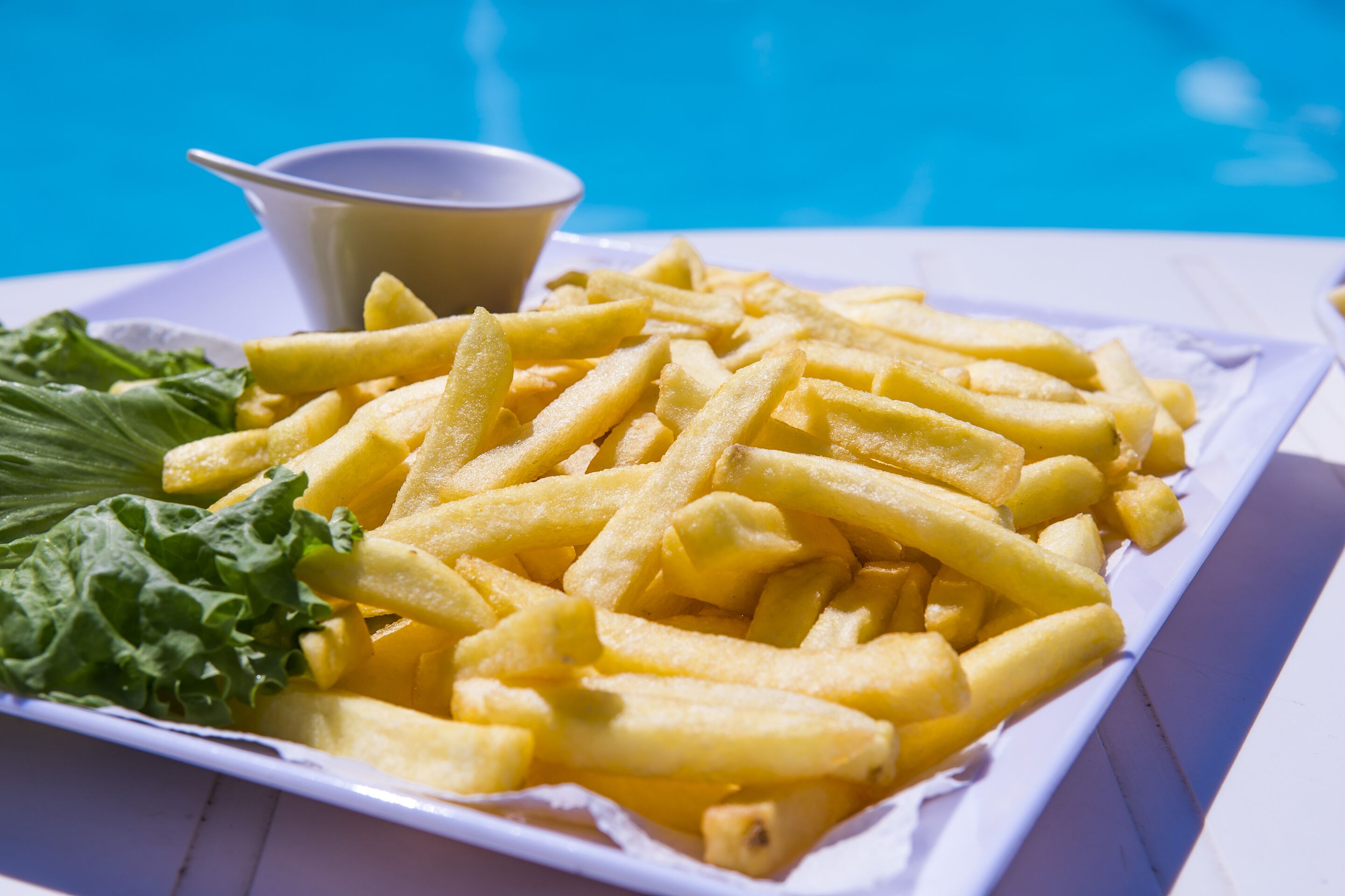 A plate of French fries with a side of greens and a small bowl of sauce.