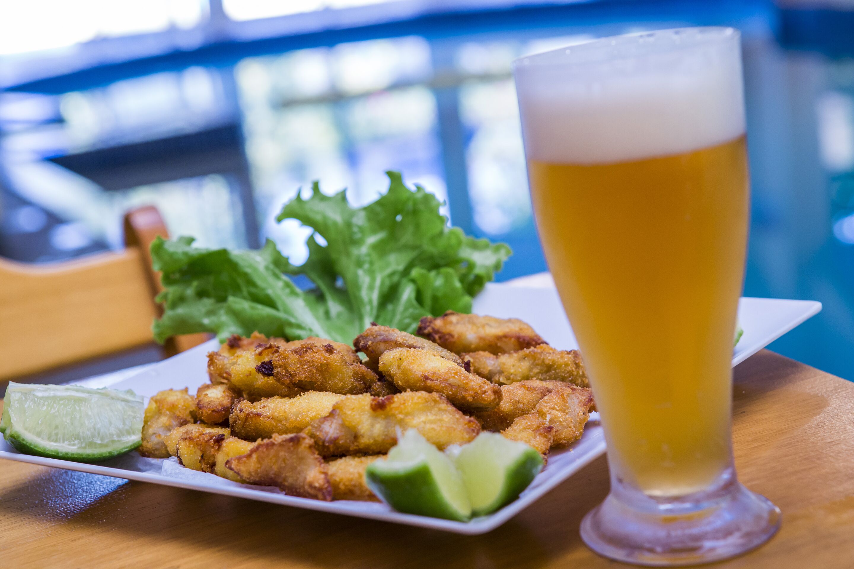 A plate of fried food with a glass of beer and a lime wedge.