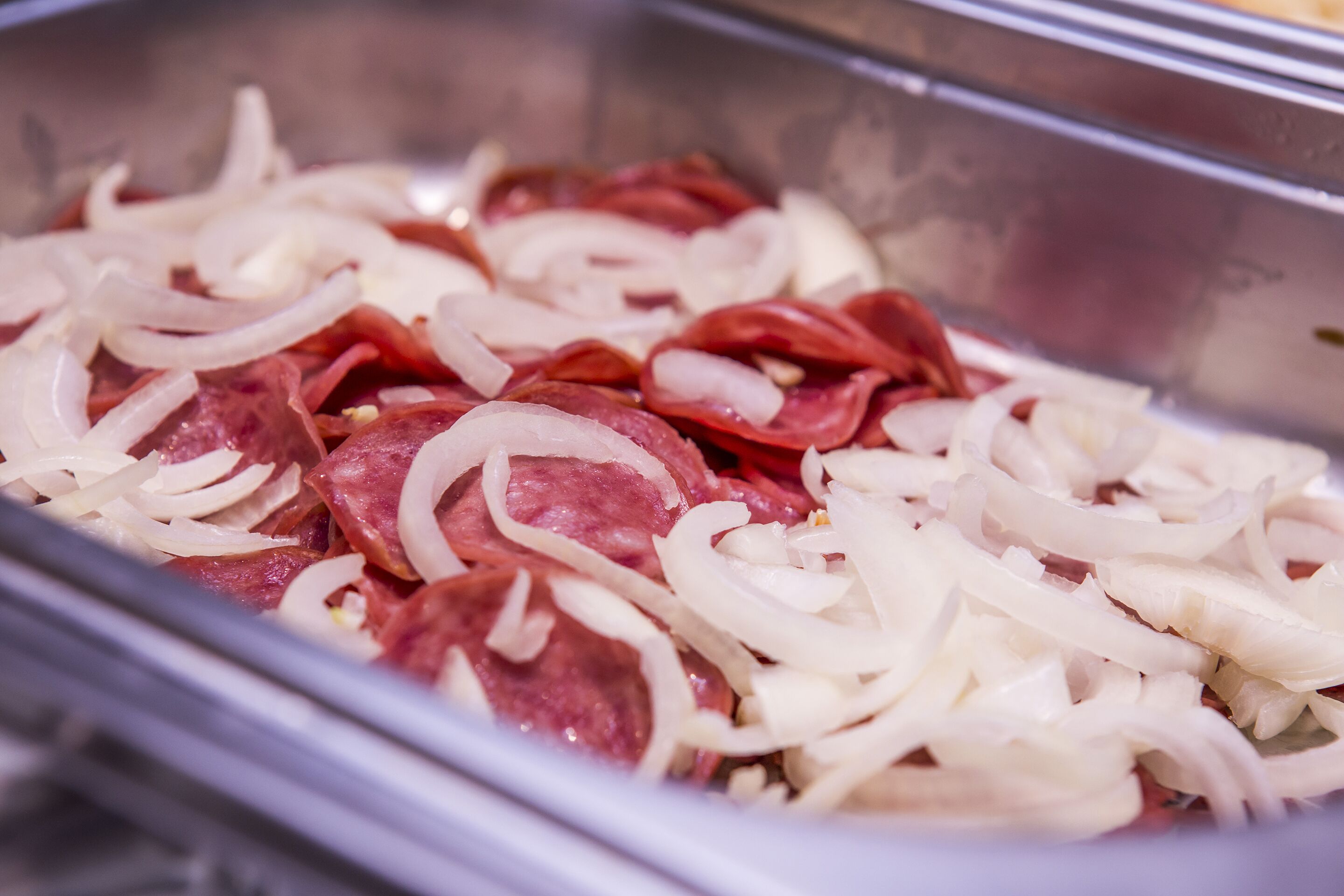 A metal tray containing sliced salami and onions.