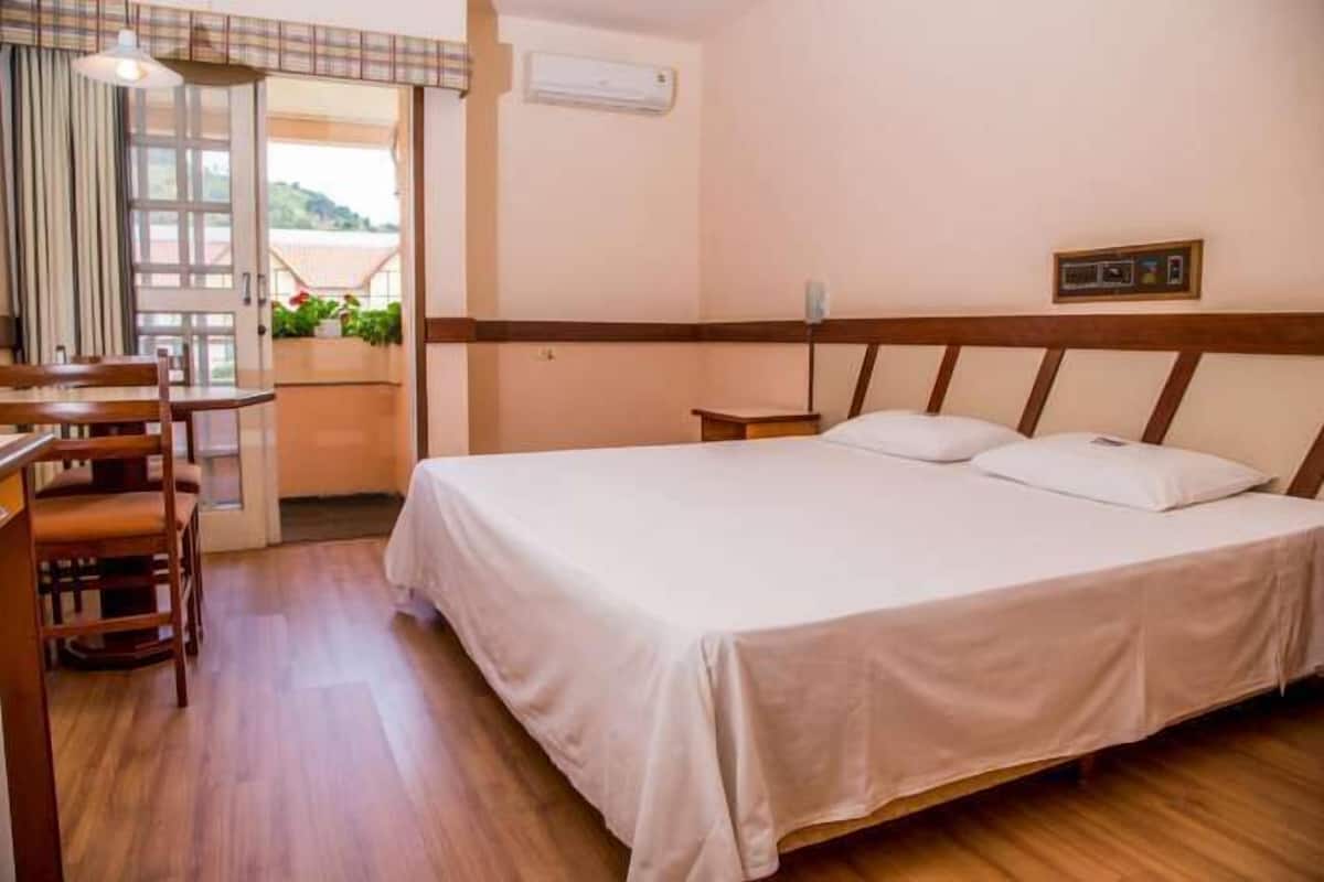 Ein Hotelzimmer mit einem Bett, einem Holztisch, einem Stuhl, einem kleinen Tisch und einem Fenster mit Vorhängen.