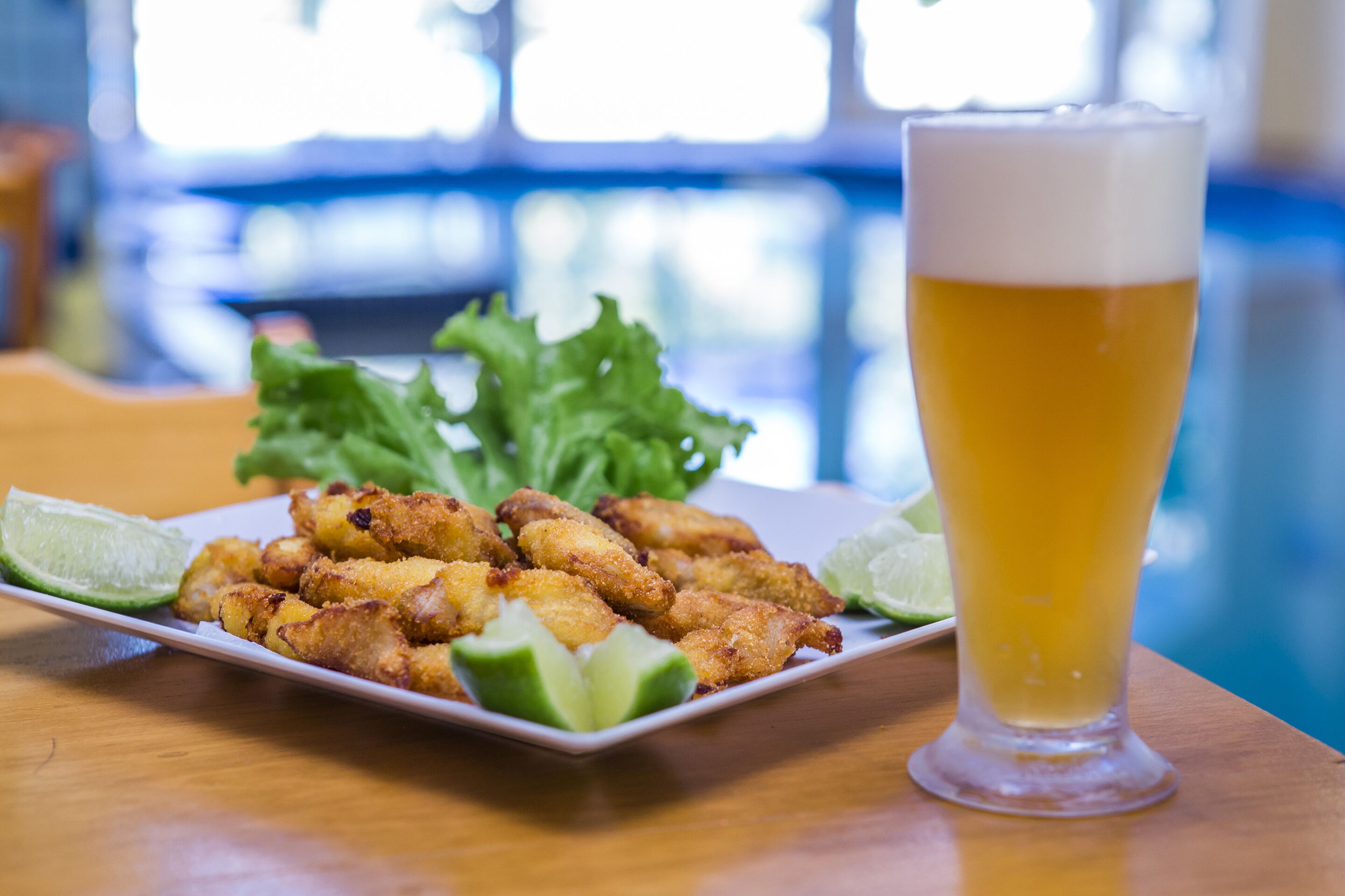 A plate of fried chicken wings with lime wedges and a glass of beer on a wooden table.