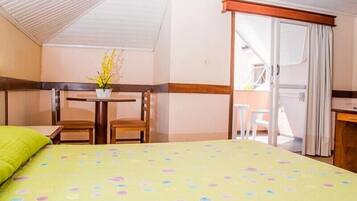 Habitación de hotel con cama, una pequeña mesa con sillas, una planta en maceta y un balcón con puerta corredera.