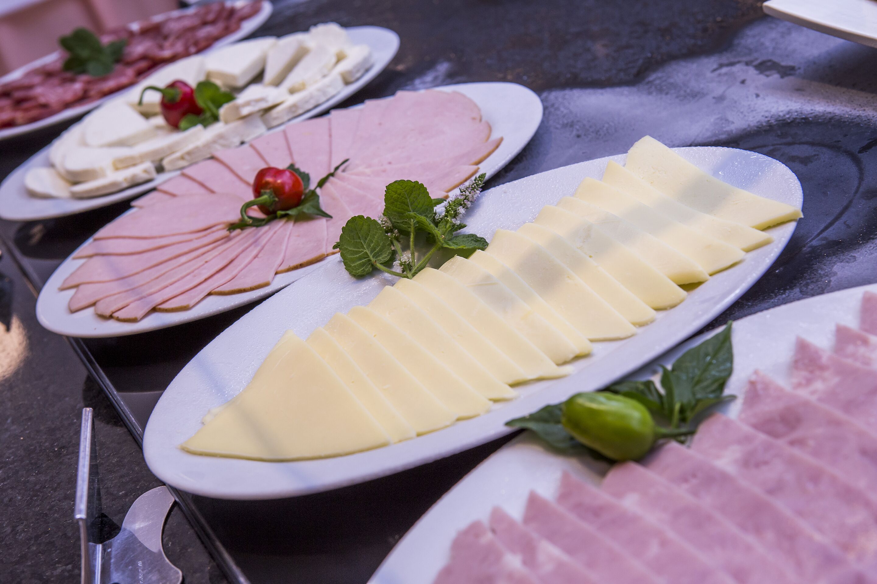 A table with various food items including sliced meats and cheeses, arranged on white plates.