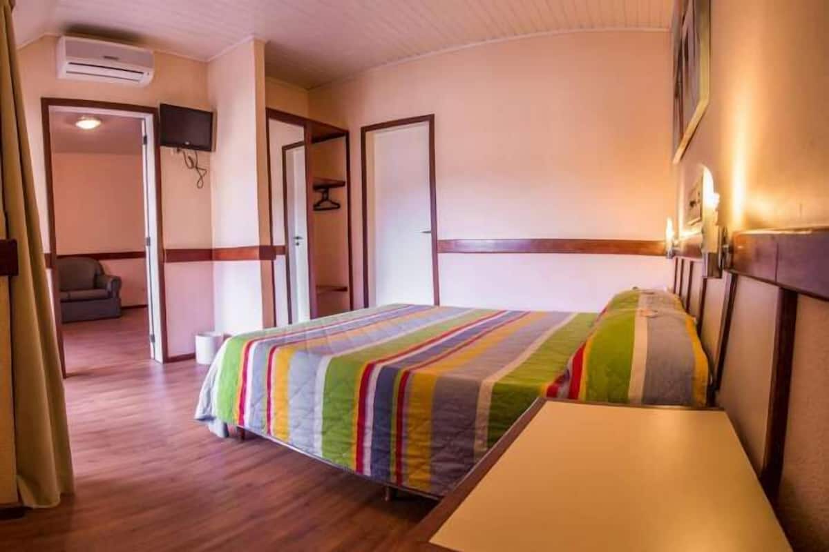 Ein Hotelzimmer mit einem Bett, einem Nachttisch, einem an der Wand befestigten Fernseher und einer Tür zu einem anderen Raum.