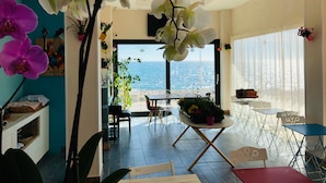 Un vaste espace de vie avec vue sur la mer, comprenant une table à manger, des chaises et des plantes en pot.