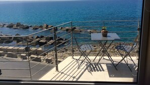 Un balcon avec vue sur la mer, une petite table avec une plante et une chaise.