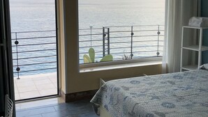 Une chambre dotée d’une grande fenêtre donnant sur un balcon avec une balustrade et offrant une vue sur la mer.